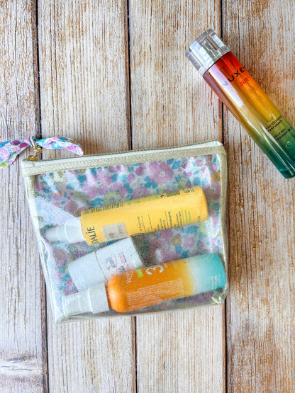 Trousse de toilette transparente Liberty avec crèmes solaires, idéale pour la plage et les vacances.