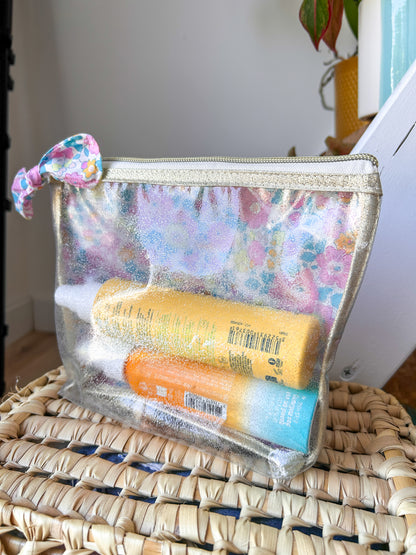 Détail d'une trousse transparente artisanale avec tissu Liberty fleuri et fermeture zippée dorée.